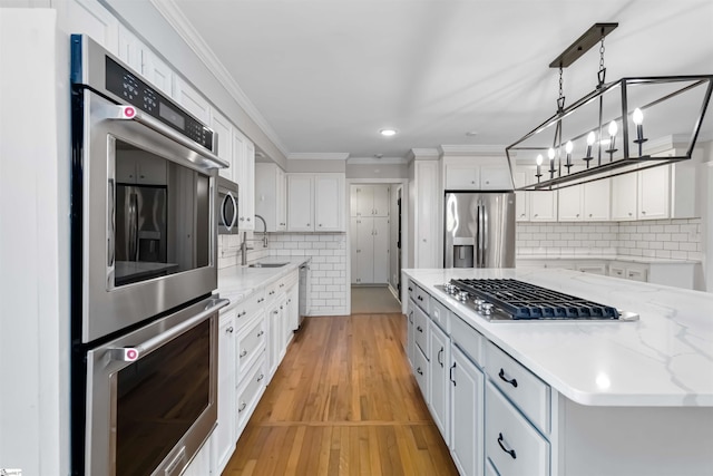 kitchen with ornamental molding, stainless steel appliances, light wood-type flooring, white cabinetry, and a sink