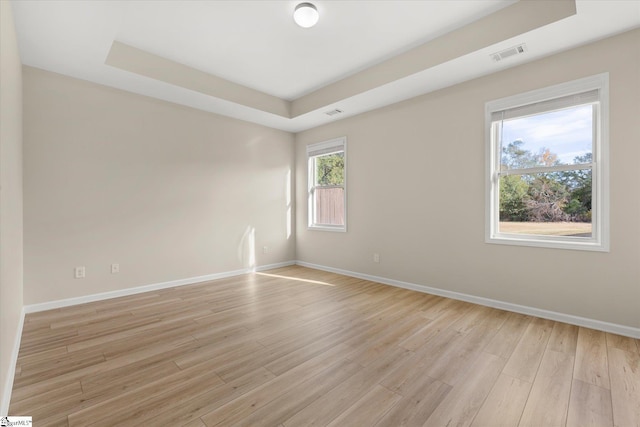 spare room featuring light wood-type flooring, baseboards, visible vents, and a raised ceiling