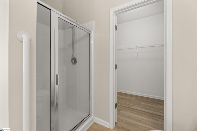 full bathroom featuring a stall shower, a walk in closet, baseboards, and wood finished floors