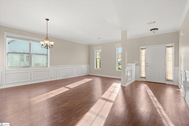 entryway with crown molding, a notable chandelier, visible vents, a decorative wall, and wood finished floors