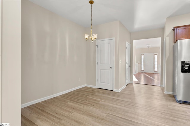 unfurnished dining area featuring an inviting chandelier, light wood-style flooring, and baseboards