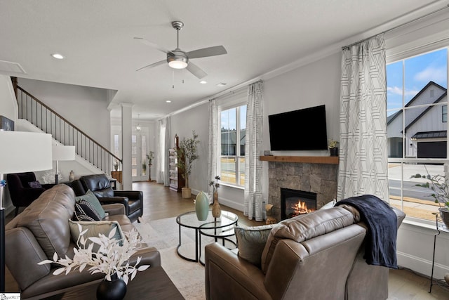 living area with a stone fireplace, ornamental molding, a ceiling fan, and wood finished floors