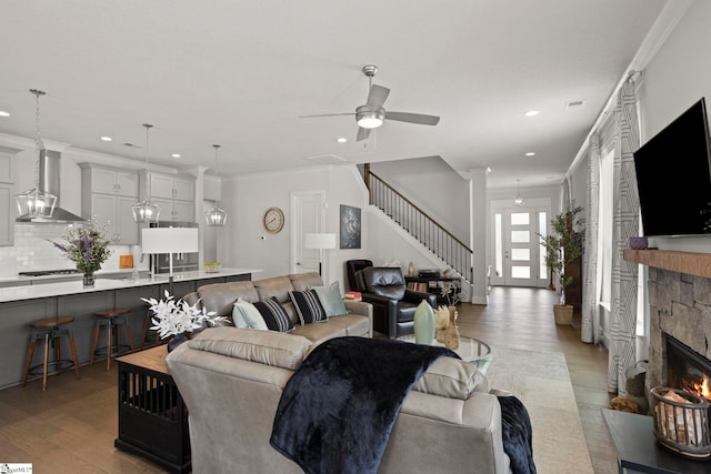 living area featuring stairway, light wood-style floors, a stone fireplace, and crown molding