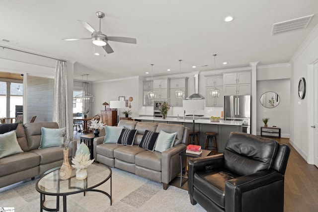 living room with light wood-type flooring, visible vents, and crown molding