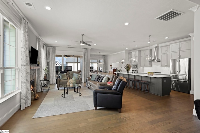 living area with recessed lighting, visible vents, a lit fireplace, and wood finished floors