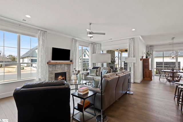 living area with visible vents, wood finished floors, a stone fireplace, baseboards, and ceiling fan