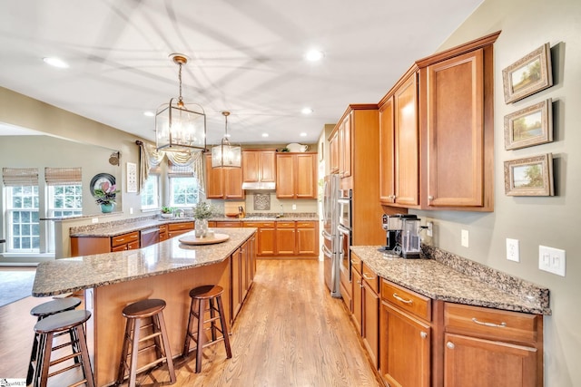 kitchen with dishwasher, light stone counters, a center island, and a kitchen breakfast bar