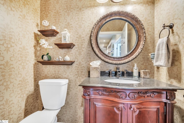 bathroom with vanity, toilet, and wallpapered walls