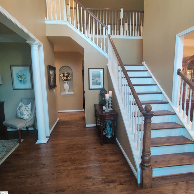 stairway with a towering ceiling, decorative columns, baseboards, and wood finished floors