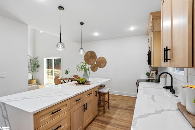 kitchen featuring light stone counters, a sink, decorative backsplash, light wood finished floors, and pendant lighting