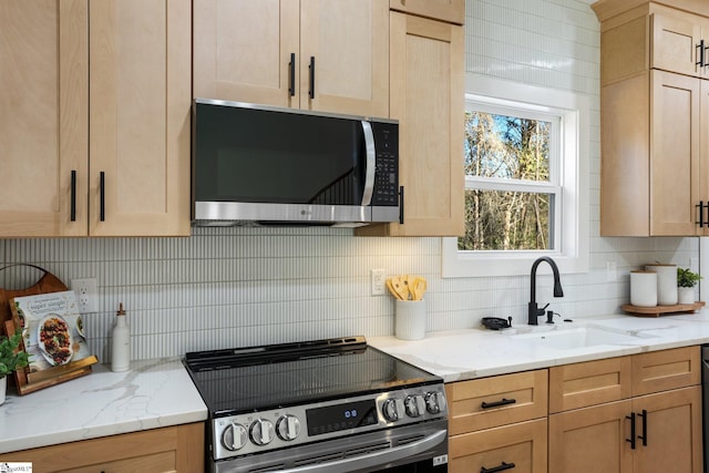 kitchen featuring stainless steel appliances, light brown cabinetry, backsplash, and a sink