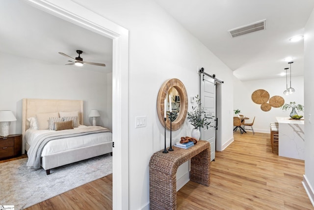 bedroom featuring a barn door, visible vents, light wood-style flooring, and baseboards