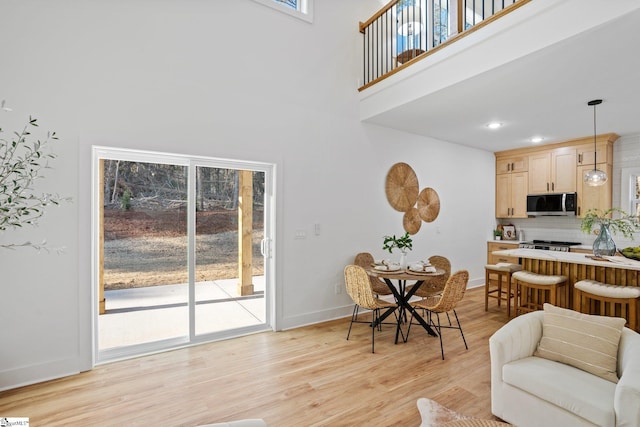 dining area featuring a towering ceiling, light wood-style flooring, baseboards, and recessed lighting