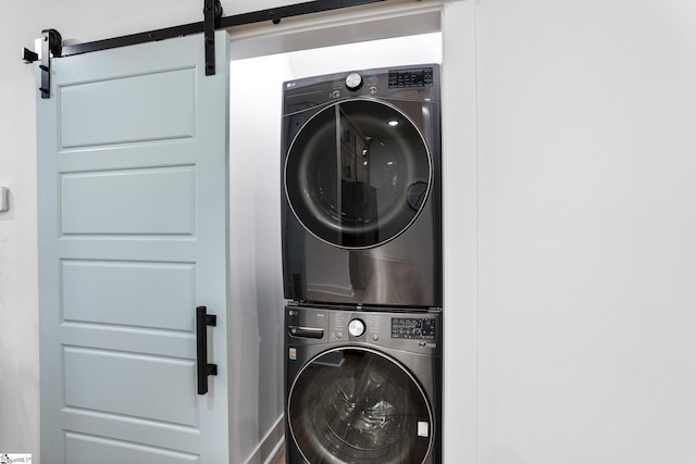 washroom with laundry area, a barn door, and stacked washing maching and dryer