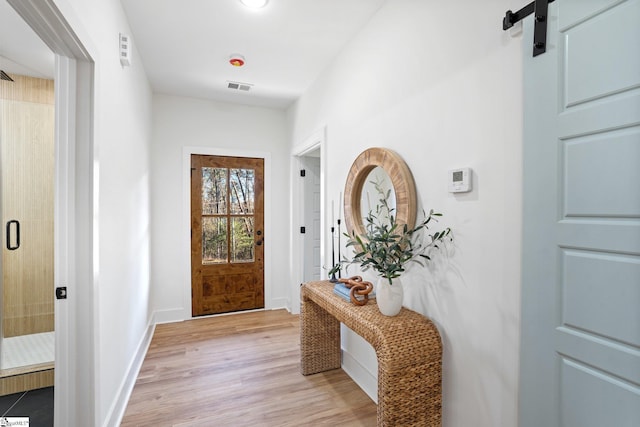 doorway to outside featuring light wood-style flooring, a barn door, visible vents, and baseboards