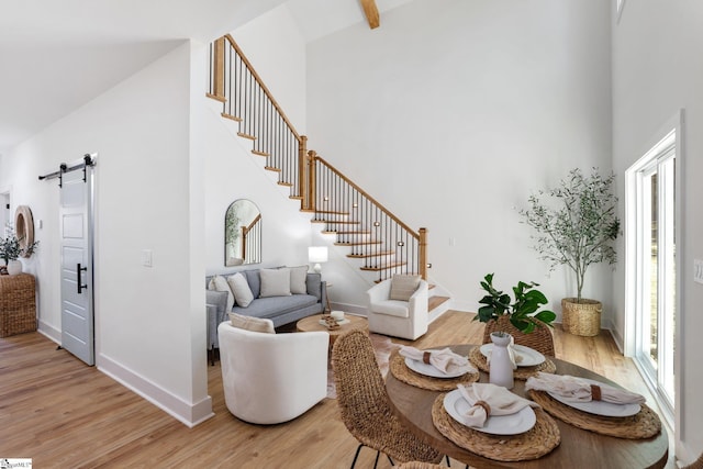 living room featuring a towering ceiling, a barn door, stairs, and light wood-style flooring