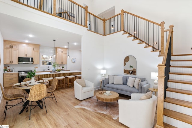 living room with a high ceiling, stairway, light wood-type flooring, and recessed lighting