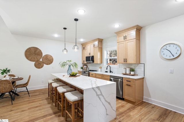 kitchen with decorative backsplash, a kitchen breakfast bar, stainless steel appliances, light wood-style floors, and a sink