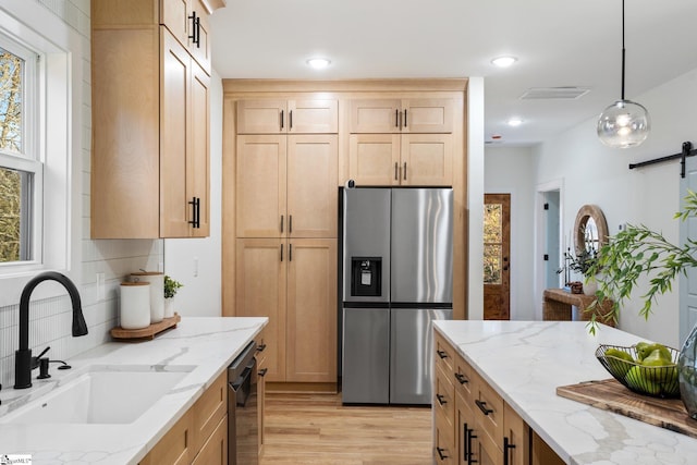 kitchen with a barn door, stainless steel appliances, a sink, visible vents, and light wood-type flooring