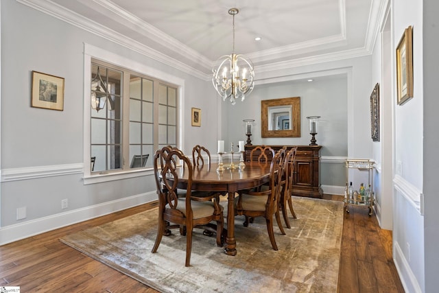 dining space featuring ornamental molding, a tray ceiling, wood-type flooring, and baseboards