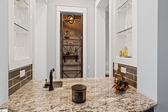 interior space with tasteful backsplash, a sink, and light stone counters