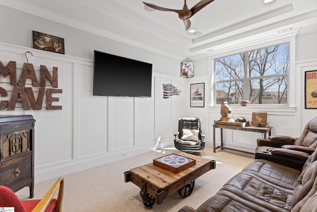 living room featuring carpet floors, visible vents, a decorative wall, and a raised ceiling