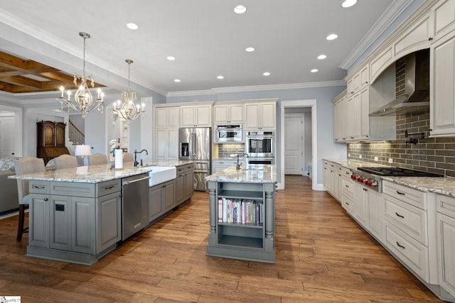 kitchen with a sink, appliances with stainless steel finishes, gray cabinets, wall chimney exhaust hood, and a large island with sink