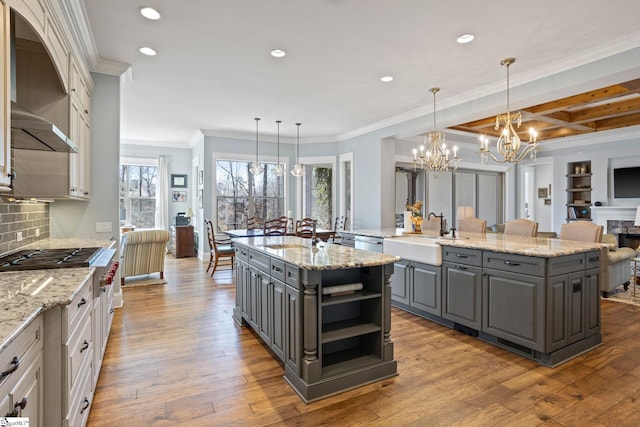 kitchen with hardwood / wood-style flooring, a large island with sink, gray cabinetry, wall chimney range hood, and a sink