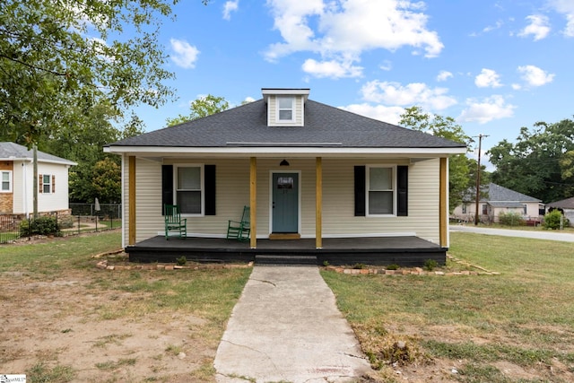 bungalow with covered porch, a shingled roof, fence, and a front lawn