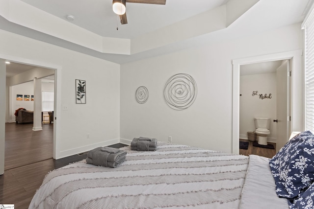 bedroom with a raised ceiling, ensuite bathroom, baseboards, and wood finished floors