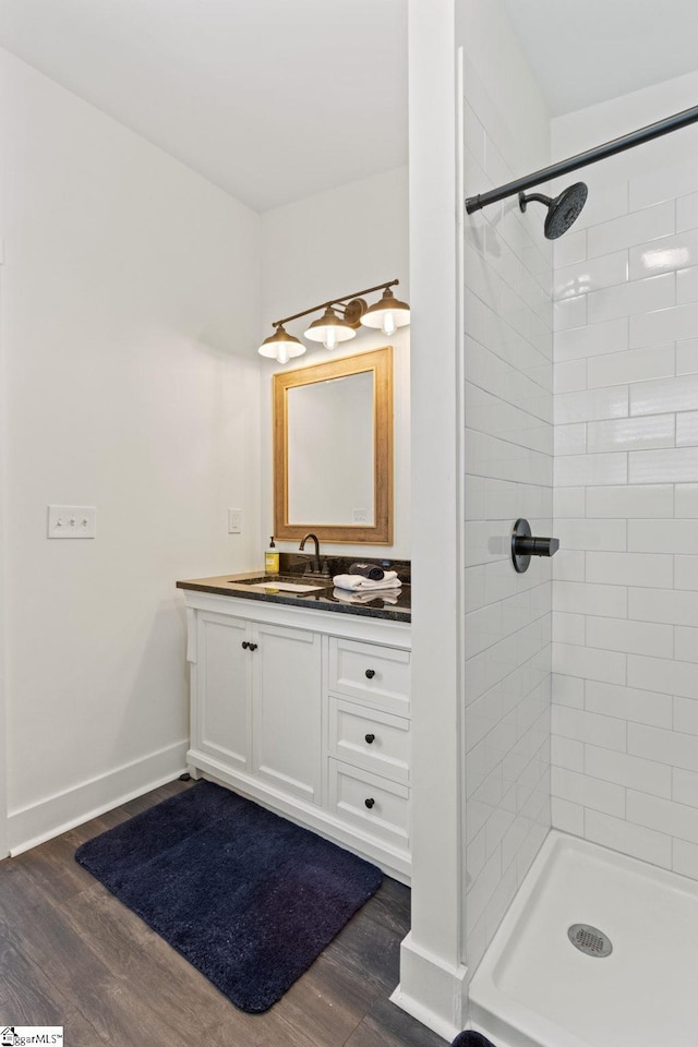 full bath featuring tiled shower, wood finished floors, vanity, and baseboards