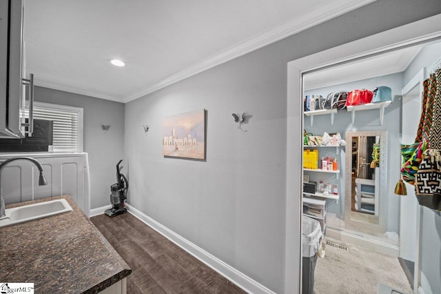 kitchen featuring baseboards, dark countertops, ornamental molding, dark wood-type flooring, and a sink