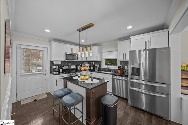 kitchen with dark countertops, appliances with stainless steel finishes, crown molding, white cabinetry, and a sink