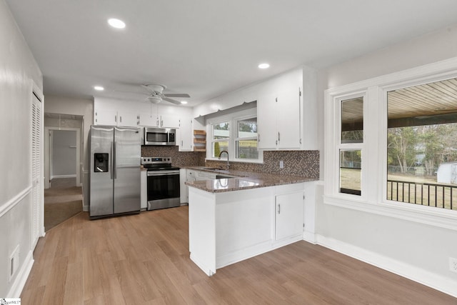 kitchen featuring a peninsula, appliances with stainless steel finishes, white cabinetry, and decorative backsplash