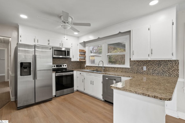 kitchen featuring white cabinets, appliances with stainless steel finishes, a peninsula, light wood-type flooring, and a sink