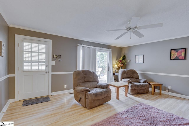 living area with ornamental molding, a ceiling fan, baseboards, and wood finished floors