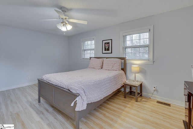 bedroom featuring a ceiling fan, light wood-style flooring, visible vents, and baseboards