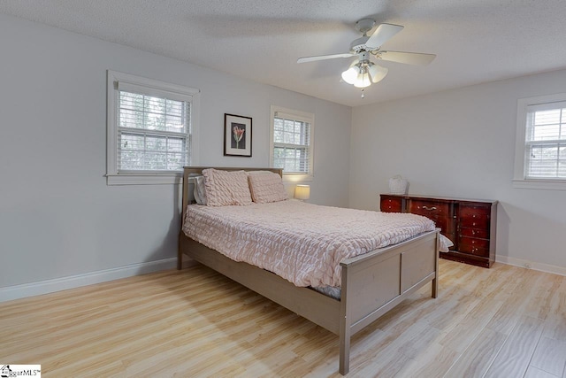 bedroom featuring light wood-style floors, ceiling fan, a textured ceiling, and baseboards