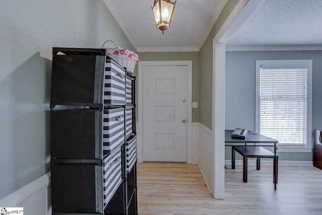 foyer featuring ornamental molding, a wainscoted wall, light wood-style flooring, and a textured ceiling