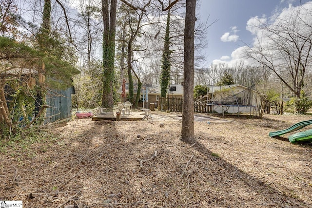 view of yard featuring a trampoline, fence, and a playground