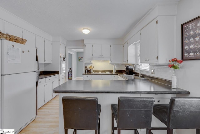 kitchen with white appliances, decorative backsplash, dark countertops, a peninsula, and a sink