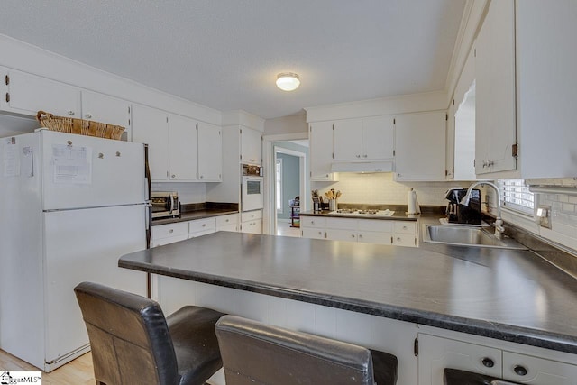 kitchen featuring dark countertops, white appliances, a sink, and a peninsula