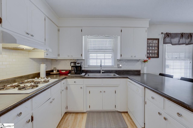 kitchen with white appliances, dark countertops, light wood-style flooring, under cabinet range hood, and a sink