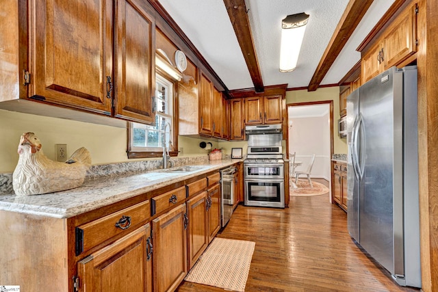kitchen with under cabinet range hood, stainless steel appliances, wood finished floors, a sink, and beamed ceiling