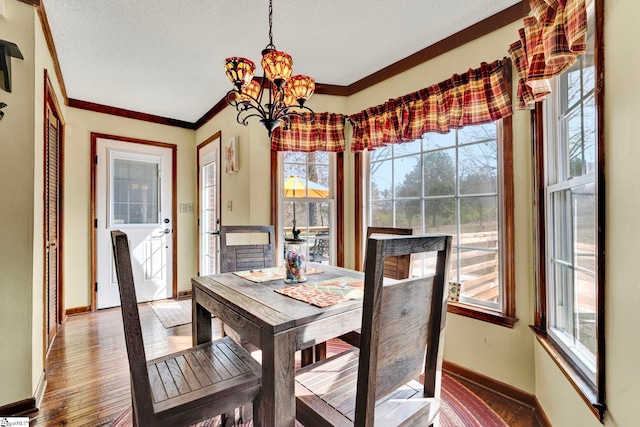 dining area featuring hardwood / wood-style floors, ornamental molding, a textured ceiling, a chandelier, and baseboards