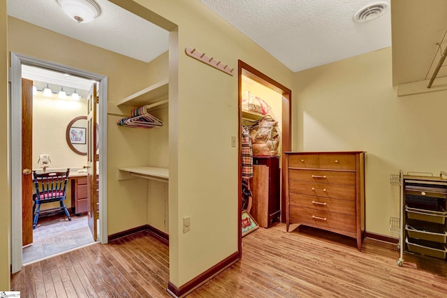 interior space with visible vents, a textured ceiling, baseboards, and wood finished floors