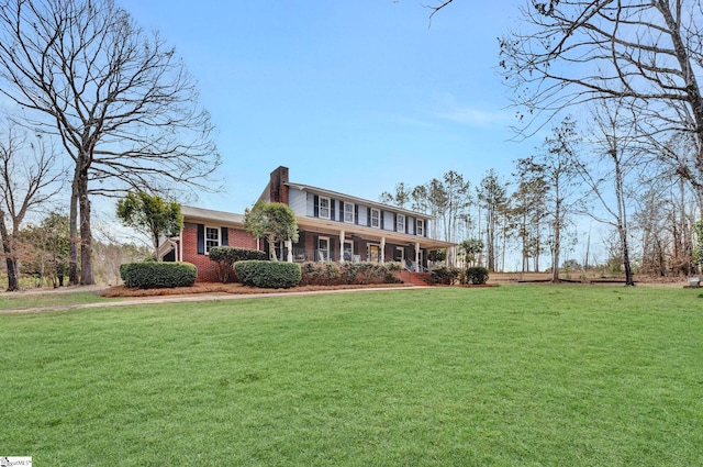 colonial home with covered porch, brick siding, a chimney, and a front yard