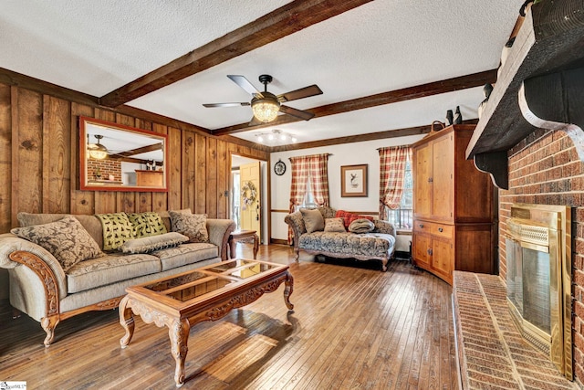 living area featuring a textured ceiling, wood walls, a brick fireplace, hardwood / wood-style floors, and beamed ceiling