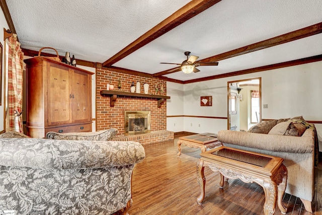 living area featuring a textured ceiling, beamed ceiling, a brick fireplace, and wood finished floors