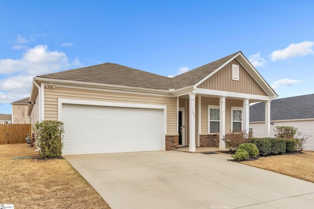 view of front of home featuring driveway, stone siding, an attached garage, covered porch, and fence